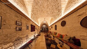 A stone-walled corridor with a high arched ceiling, seating areas with cushions, and a long table with chairs. - Michel House (Nazareth)