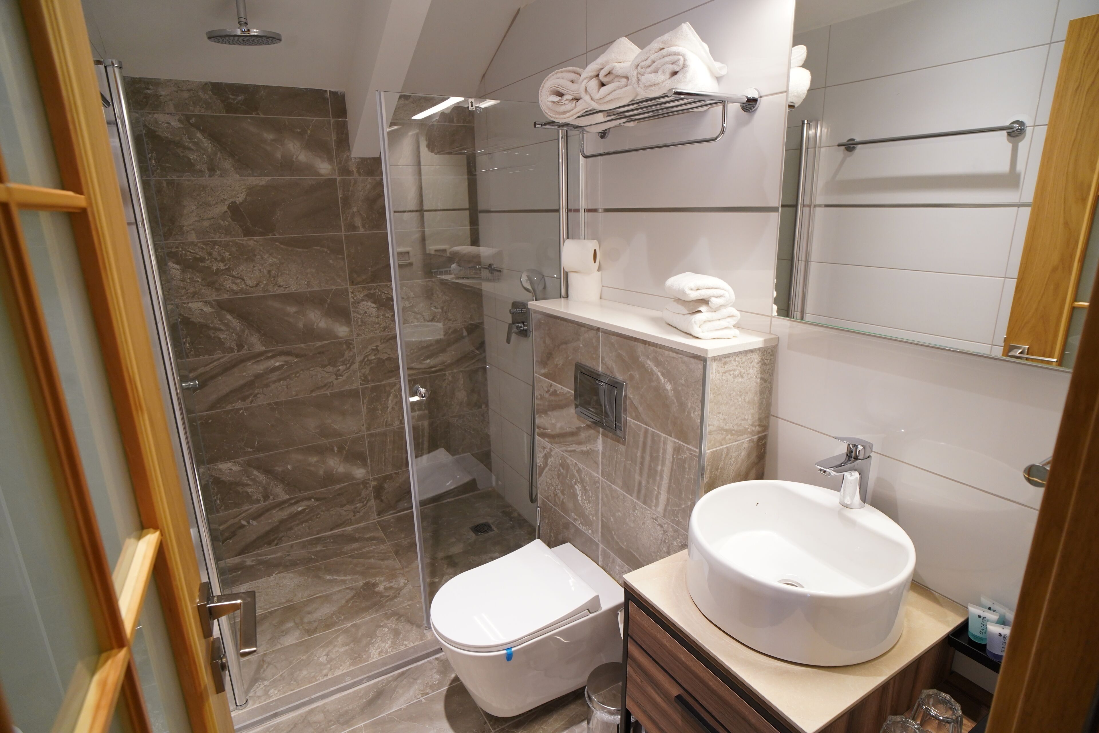 A modern bathroom with a glass-enclosed shower, a toilet, and a sink with a mirror above.