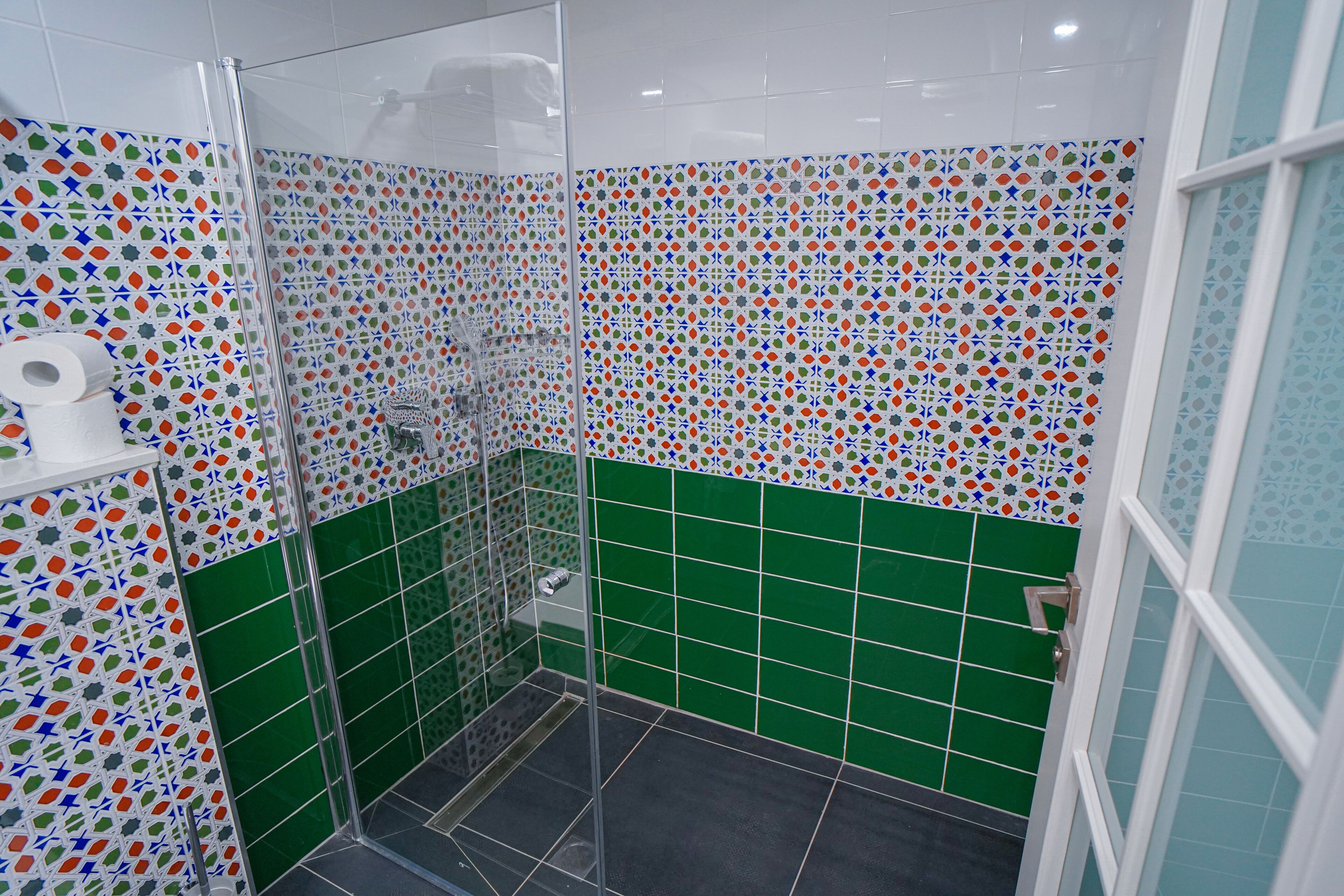 A bathroom with colorful mosaic tiles, a glass shower enclosure, and a green tiled floor.