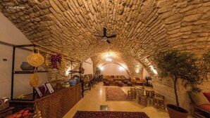 An interior with a stone ceiling, a ceiling fan, a seating area with sofas and chairs, and a potted plant. - Michel House (Nazareth)