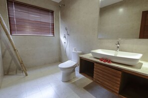 A bathroom with a toilet, a shower, a sink, and a window with blinds. - Jati Cottage (Ubud)