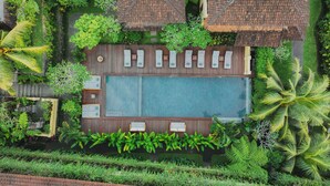 An aerial view of a resort with a central pool, surrounded by lush greenery and multiple bungalow-style accommodations with thatched roofs. - Jati Cottage (Ubud)