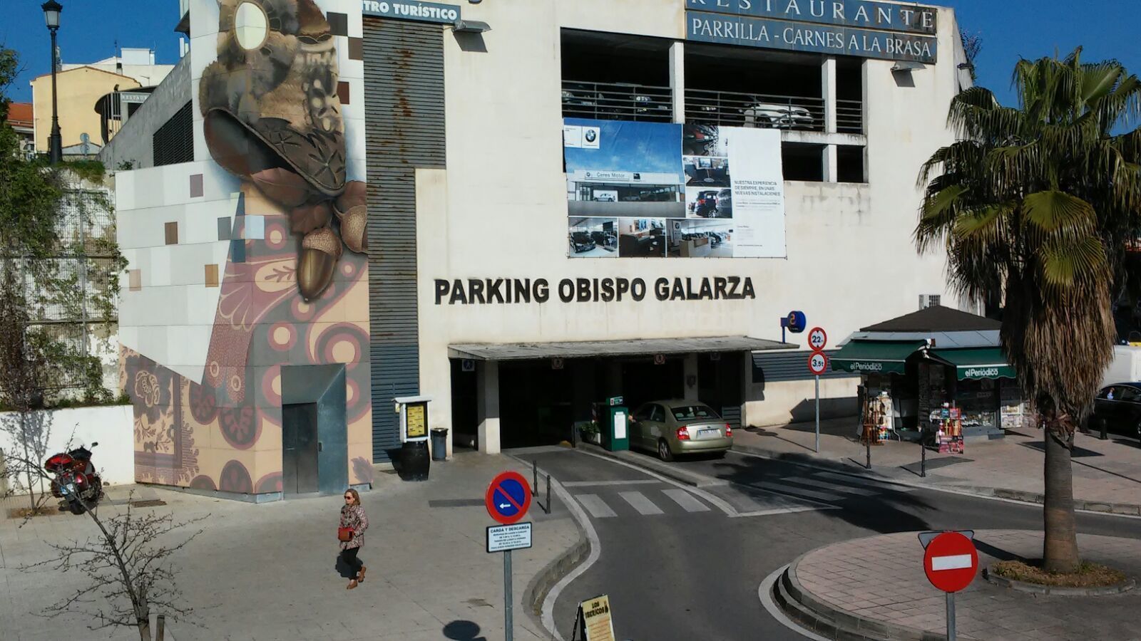 Un edificio con un mural grande, la entrada de un estacionamiento y un letrero de restaurante.