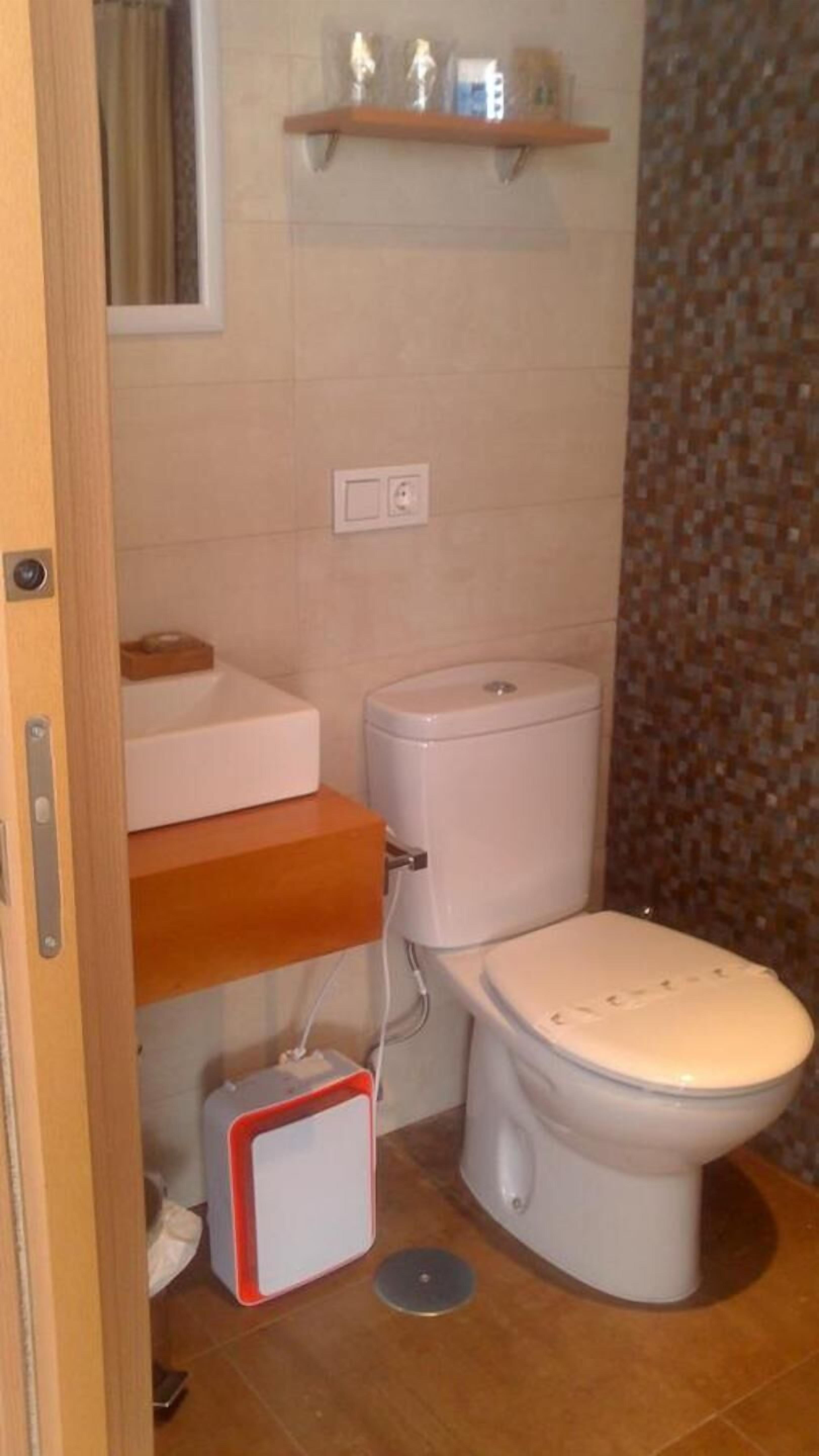 Ba ño con inodoro, lavabo y repisa sobre el inodoro.