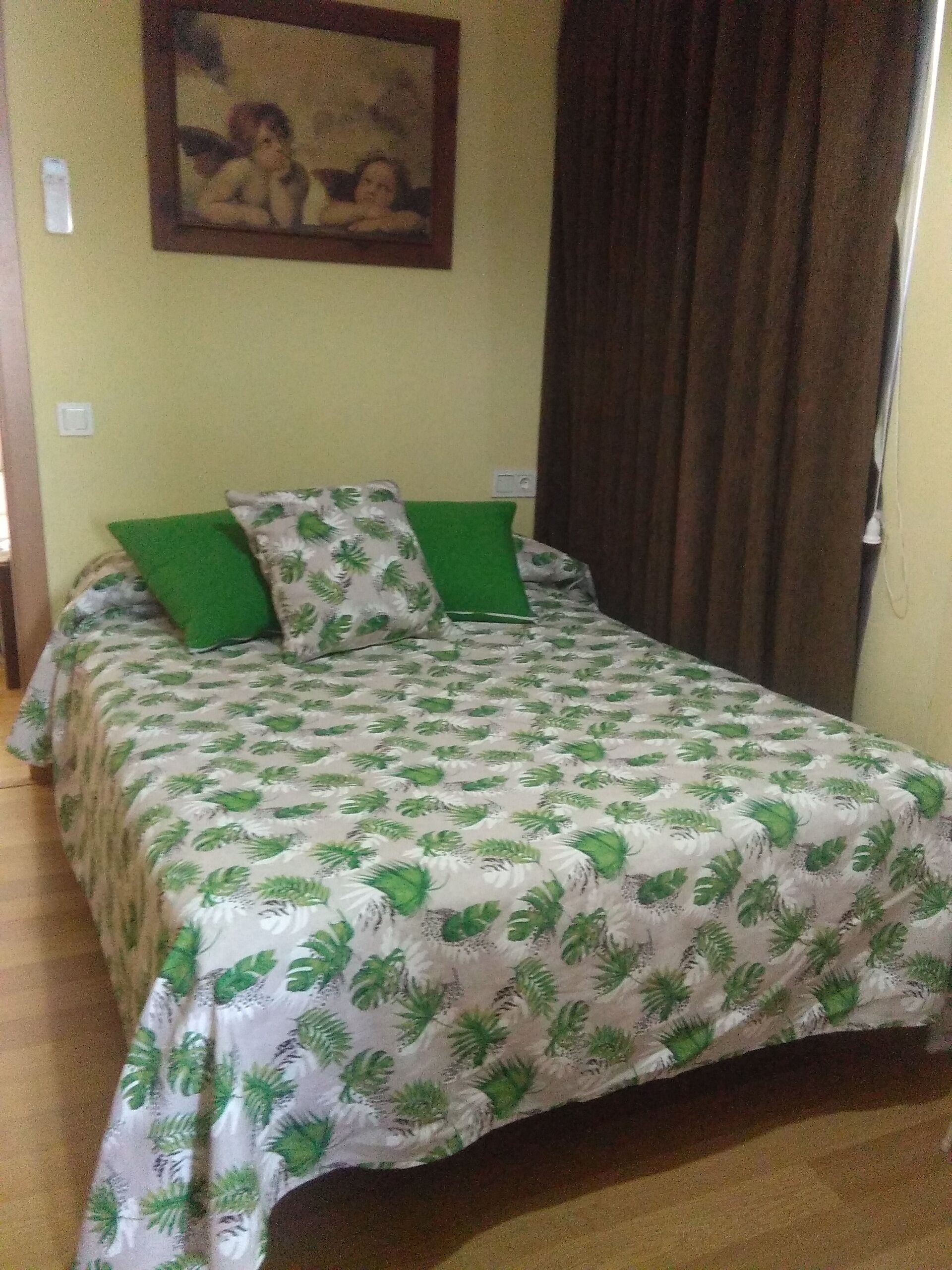 Una cama con una colcha estampada con flores, dos almohadas verdes y un cuadro en la pared.