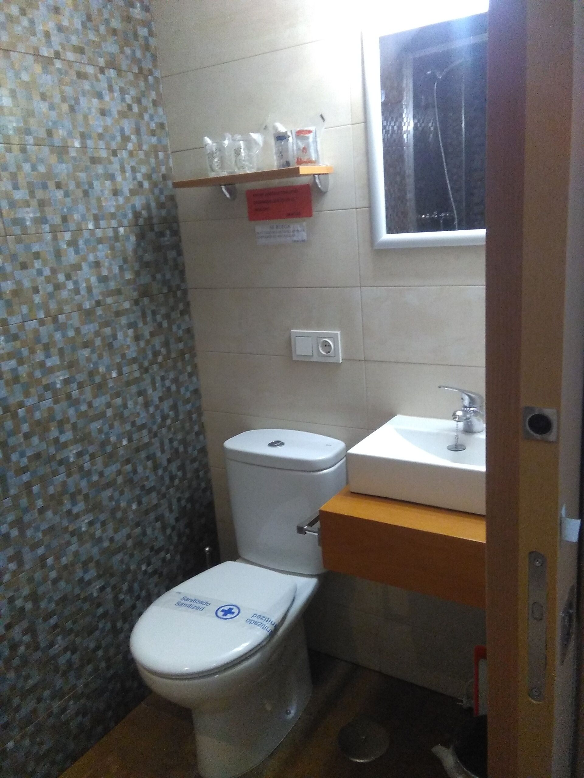 A small bathroom with a toilet, a sink, and a shelf above the toilet.