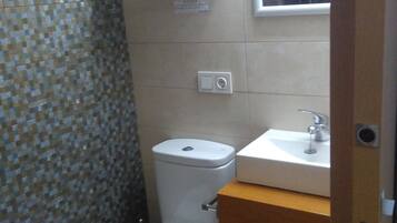 A small bathroom with a toilet, a sink, and a shelf above the toilet.