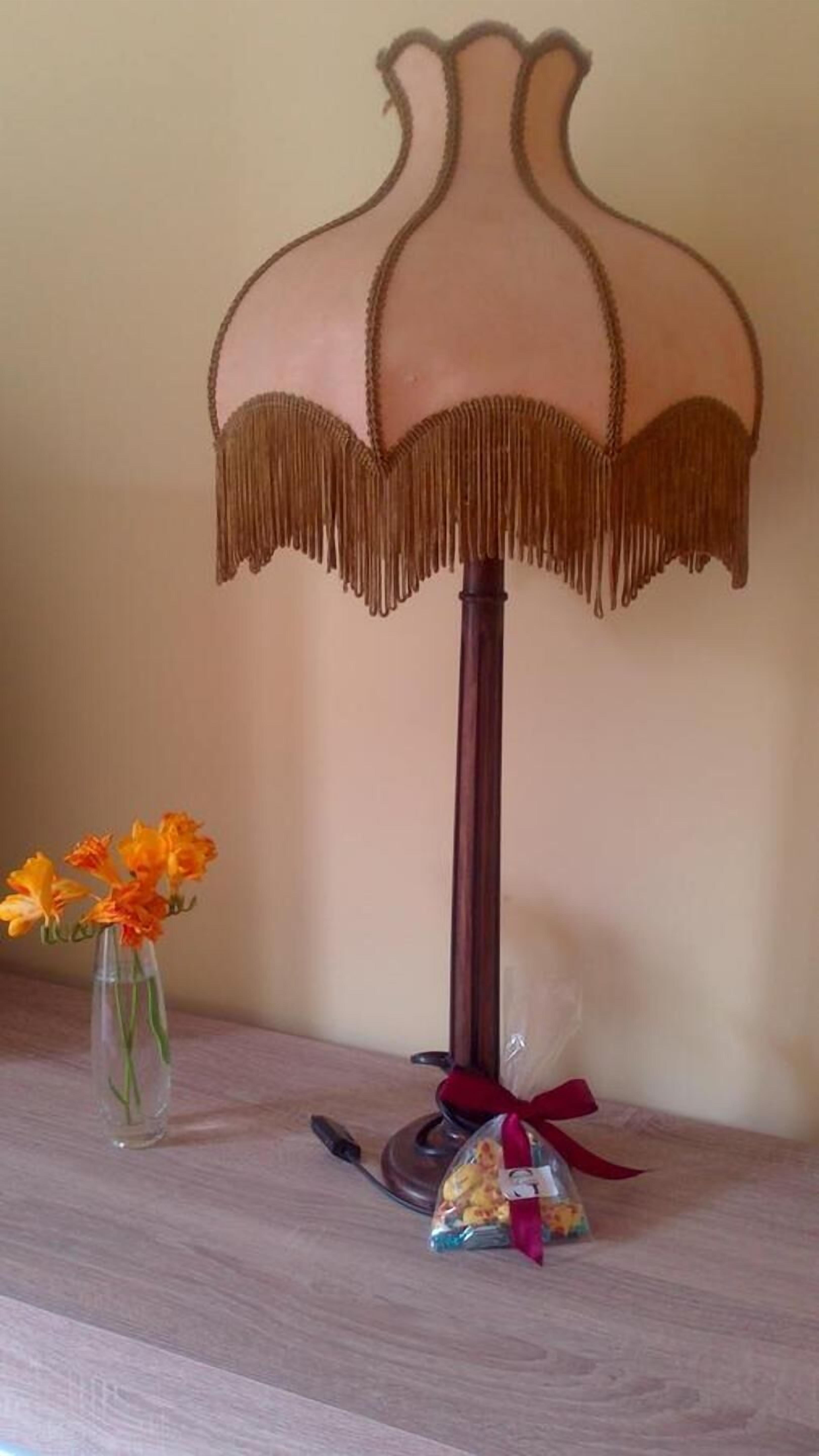 Um abajur com cúpula decorativa e um vaso com flores sobre uma superfície de madeira.