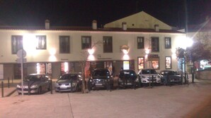 A building with multiple parked cars in front, a signboard, and a well-lit entrance. - Apartamentos Turísticos La Garza (Cáceres)