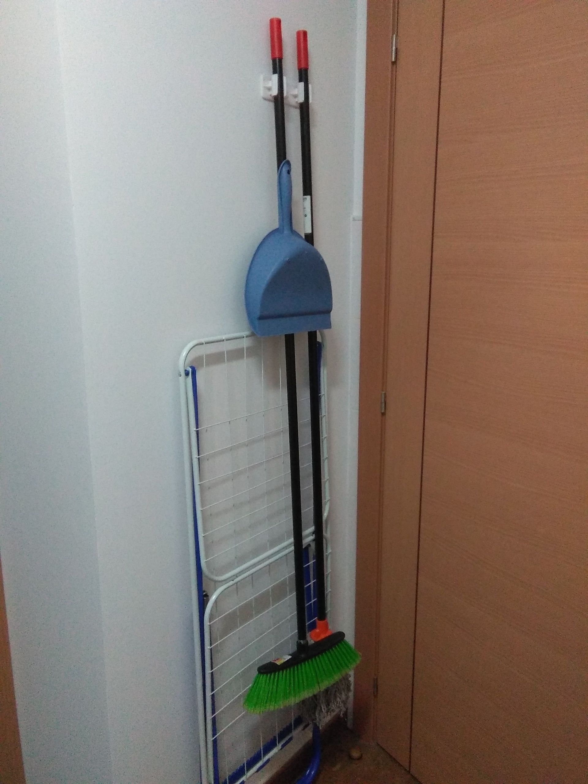 A broom and dustpan rack in a hallway.