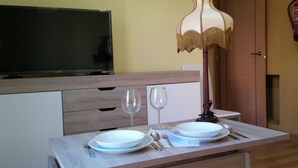 A dining area with a wooden table set for two, two white plates, two wine glasses, and a candle holder. - Apartamentos Turísticos La Garza (Cáceres)