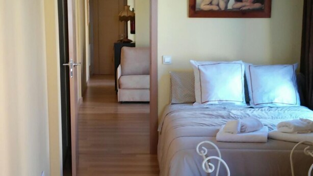 A hotel room with a bed, a chair, a painting on the wall, and a hallway leading to another room. - Apartamentos Turísticos La Garza (Cáceres)