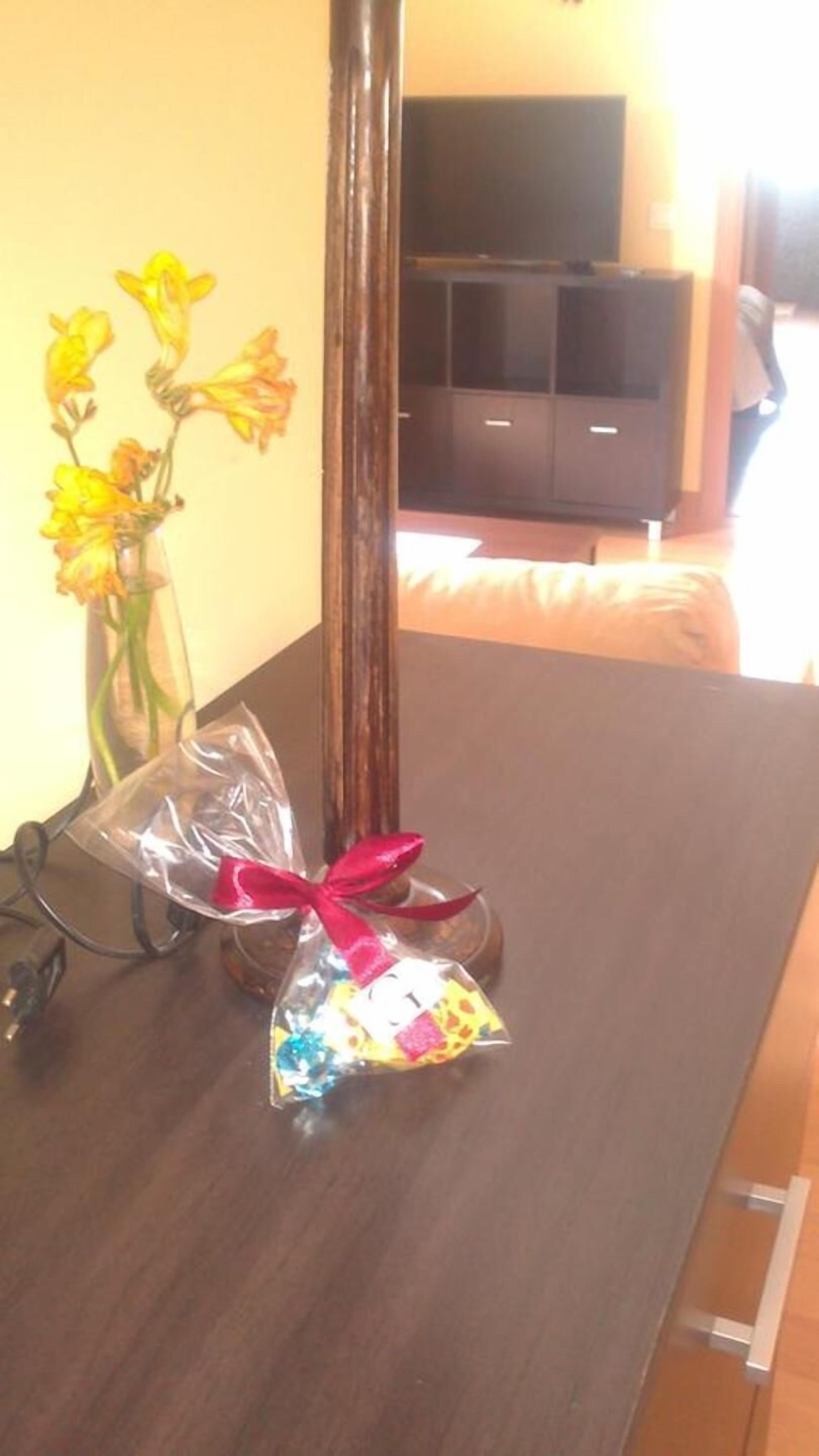 Uma mesa de madeira com um vaso de flores amarelas e uma sacola de presente com laço vermelho.