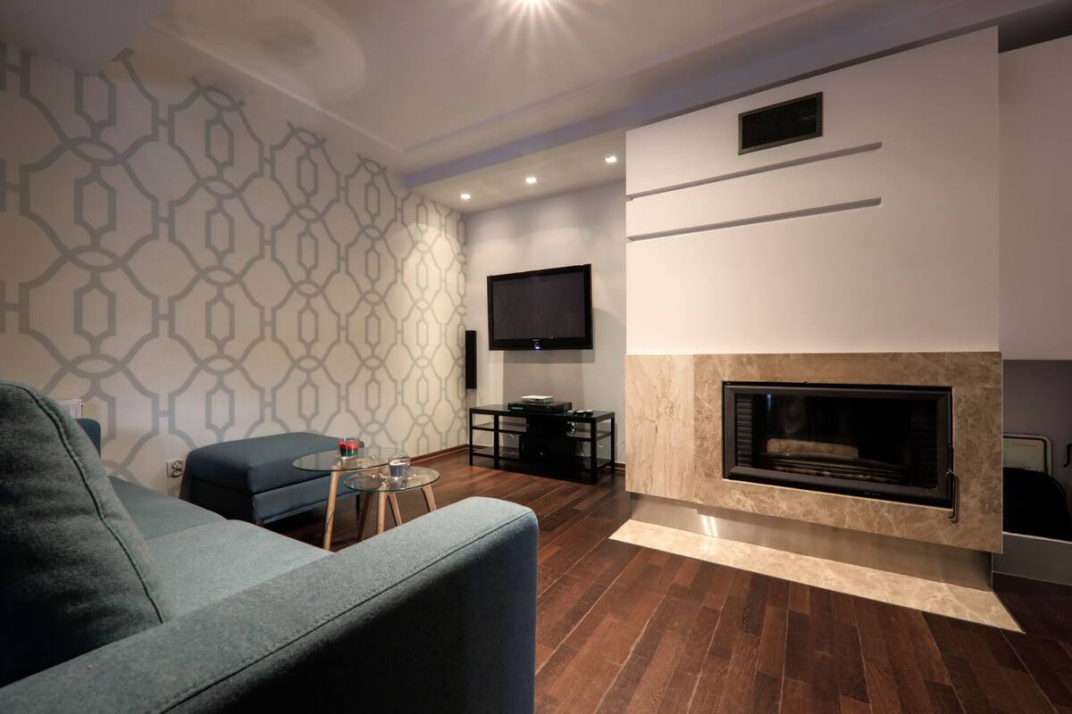 A modern living room with a sofa, a coffee table, a fireplace, and a flat-screen TV mounted on the wall.