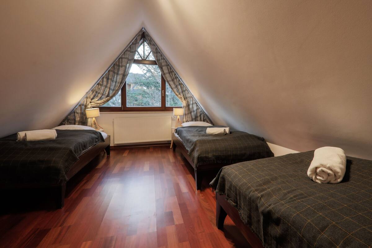 A triangular attic bedroom with two beds, a window, and a radiator.