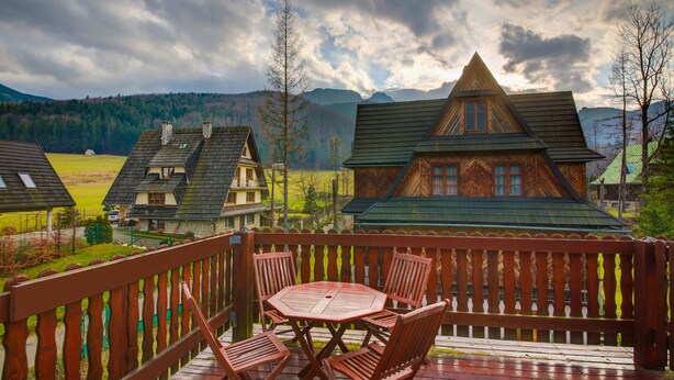 Une terrasse en bois avec une table et des chaises, offrant une vue sur un paysage montagneux parsemé de maisons traditionnelles.