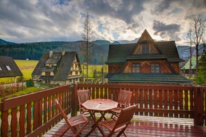 A wooden deck with a table and chairs, overlooking a mountainous landscape with traditional houses. - RentPlanet - Śpiący Rycerz (Zakopane)