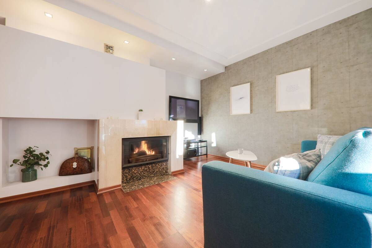 A modern living room with a fireplace, a blue sofa, and a dining area.