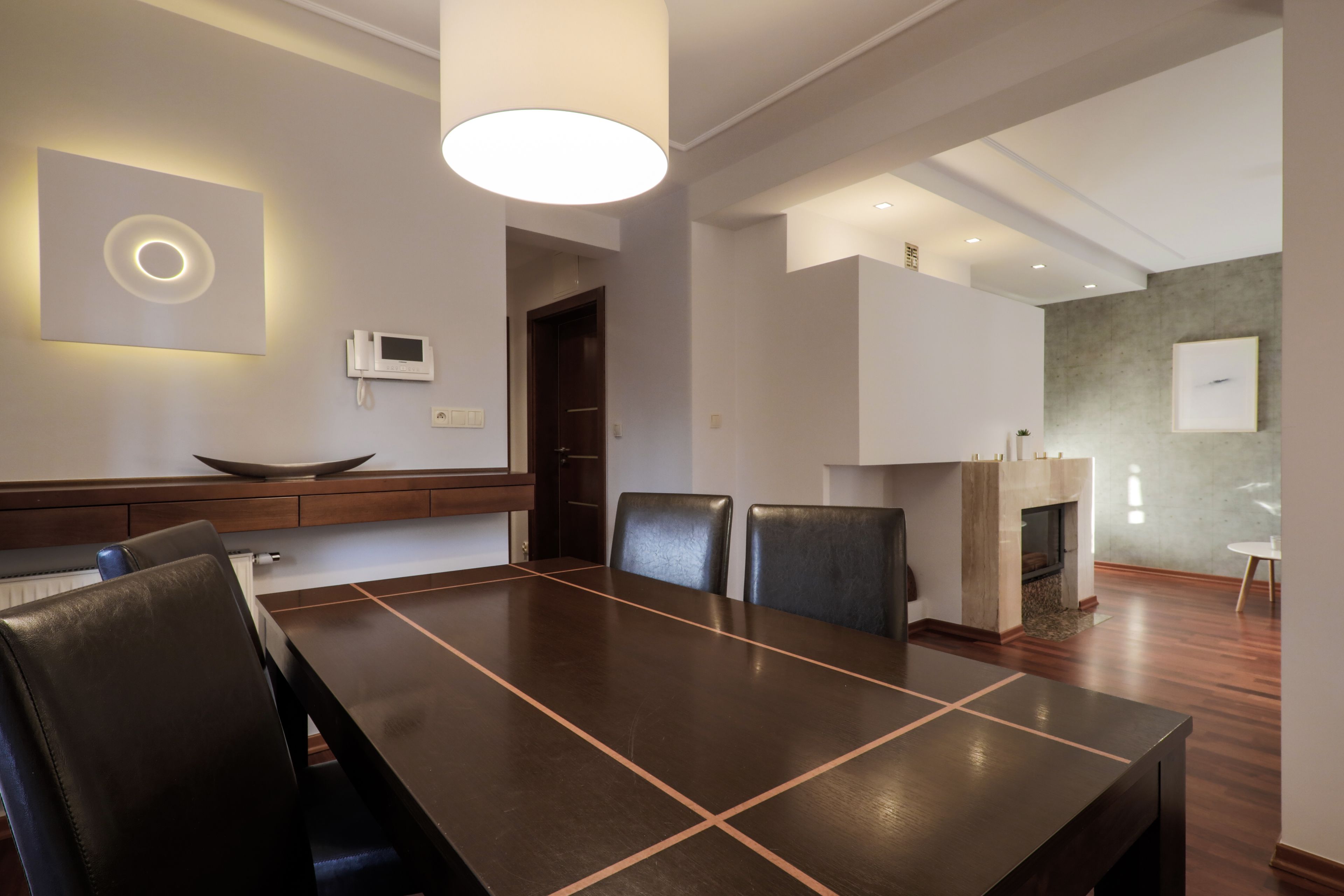 Un espace repas moderne avec une longue table, des chaises en cuir, un banc intégré, un téléphone fixé au mur et une cheminée.