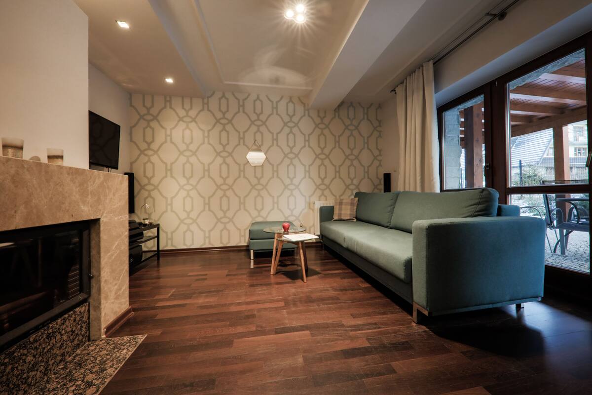 A modern living room with a fireplace, a green sofa, and a patterned wall.
