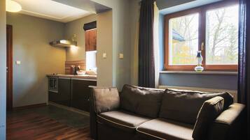 A living room with a brown leather sofa, a kitchen area with modern appliances, and a window with curtains.