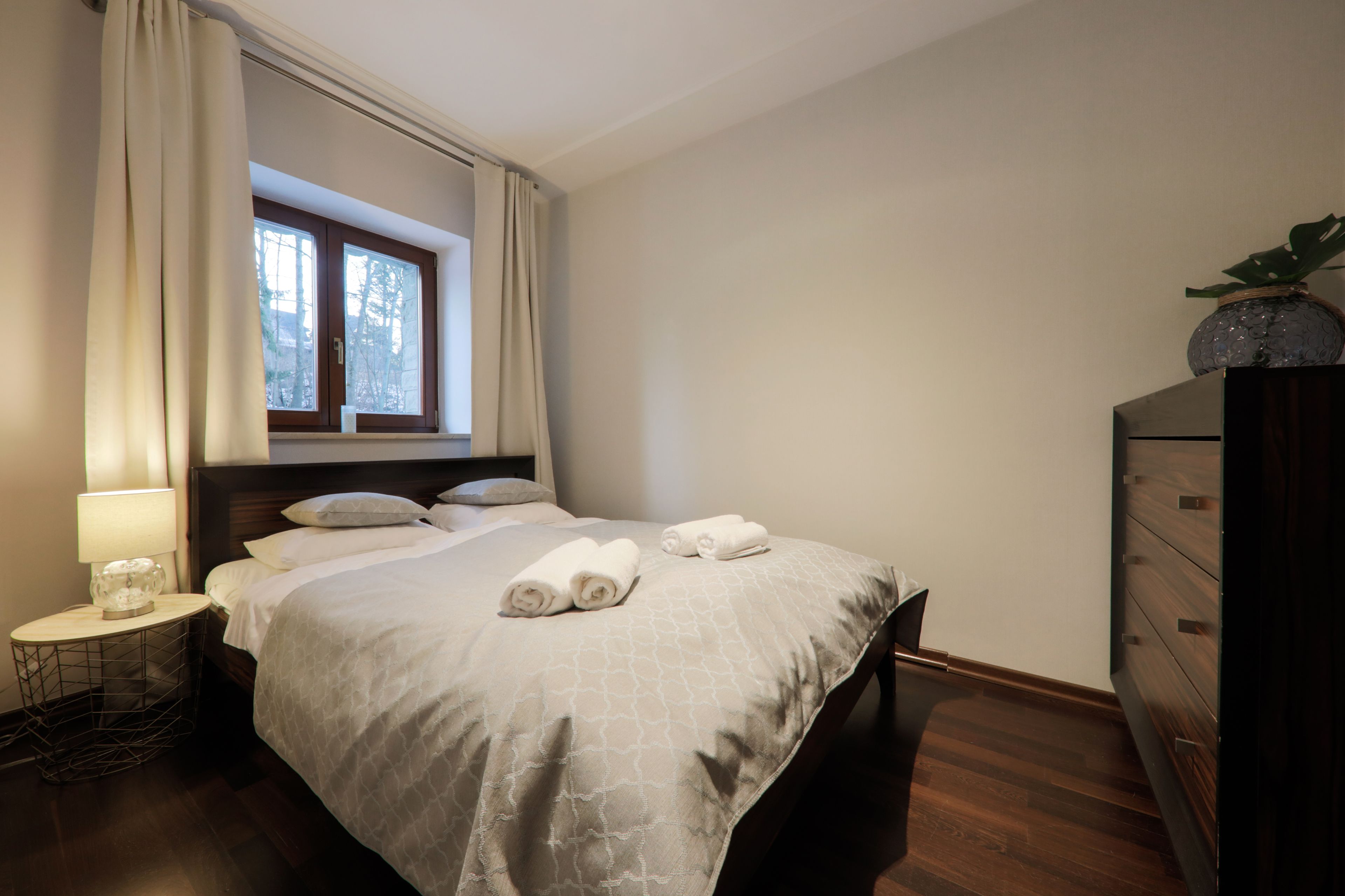 Una cama bien hecha con toallas, una lámpara de noche y una ventana con cortinas.
