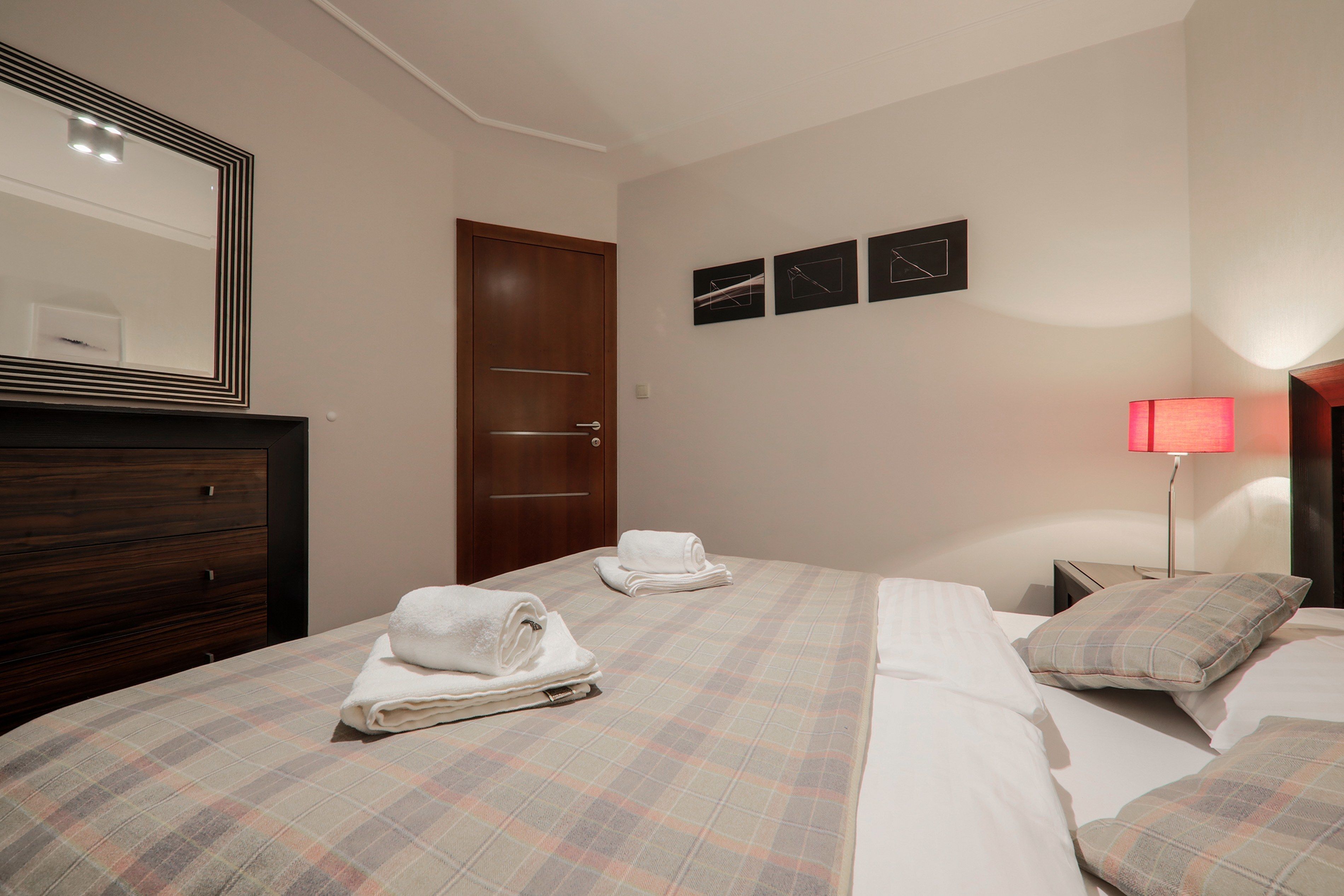 A hotel room with two beds, a wooden dresser, a mirror, and a red lamp.