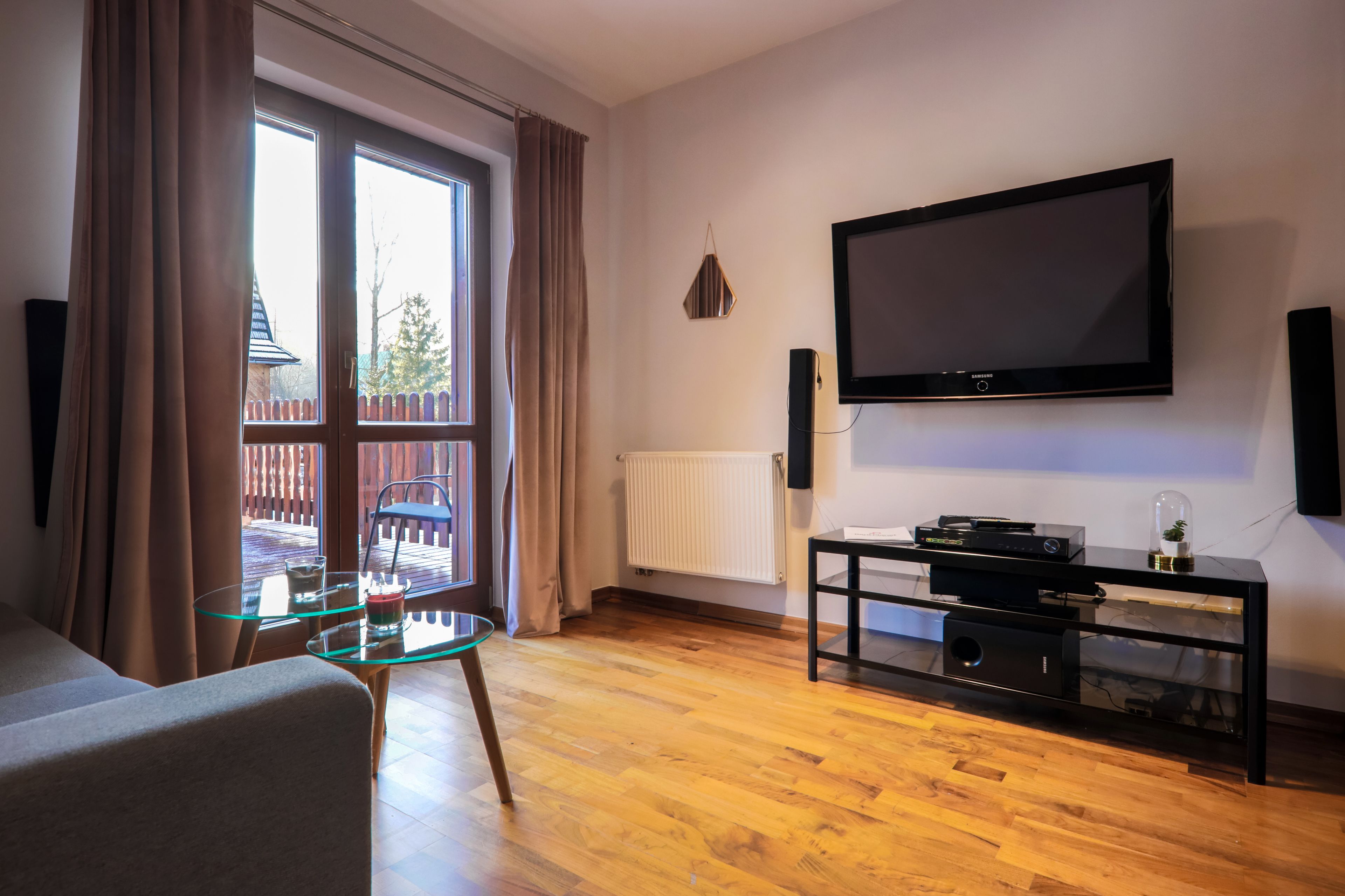Una sala de estar con un ventanal grande, un televisor de pantalla plana, una mesa de centro de vidrio y un mueble de entretenimiento negro.