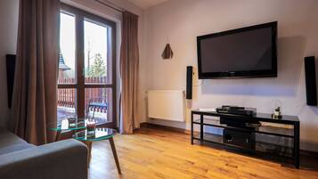 Una sala de estar con un ventanal grande, un televisor de pantalla plana, una mesa de centro de vidrio y un mueble de entretenimiento negro.