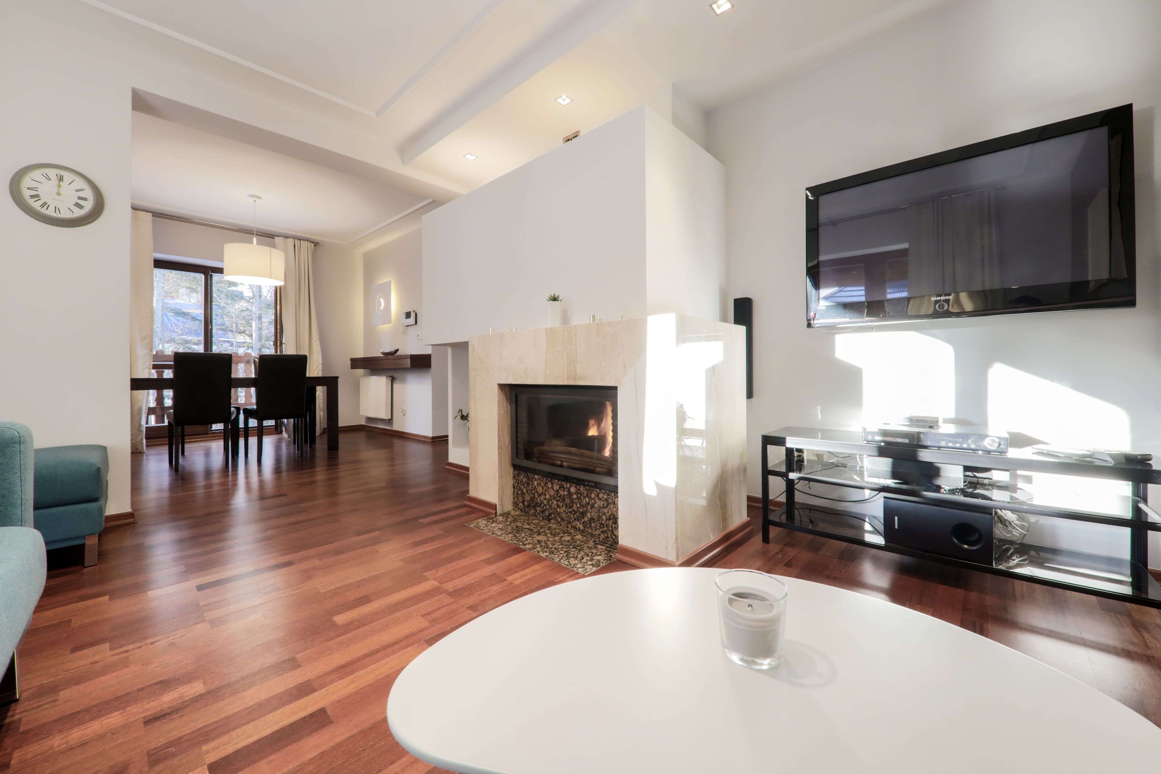 A modern living room with a fireplace, a dining area, and a flat-screen TV mounted on the wall.