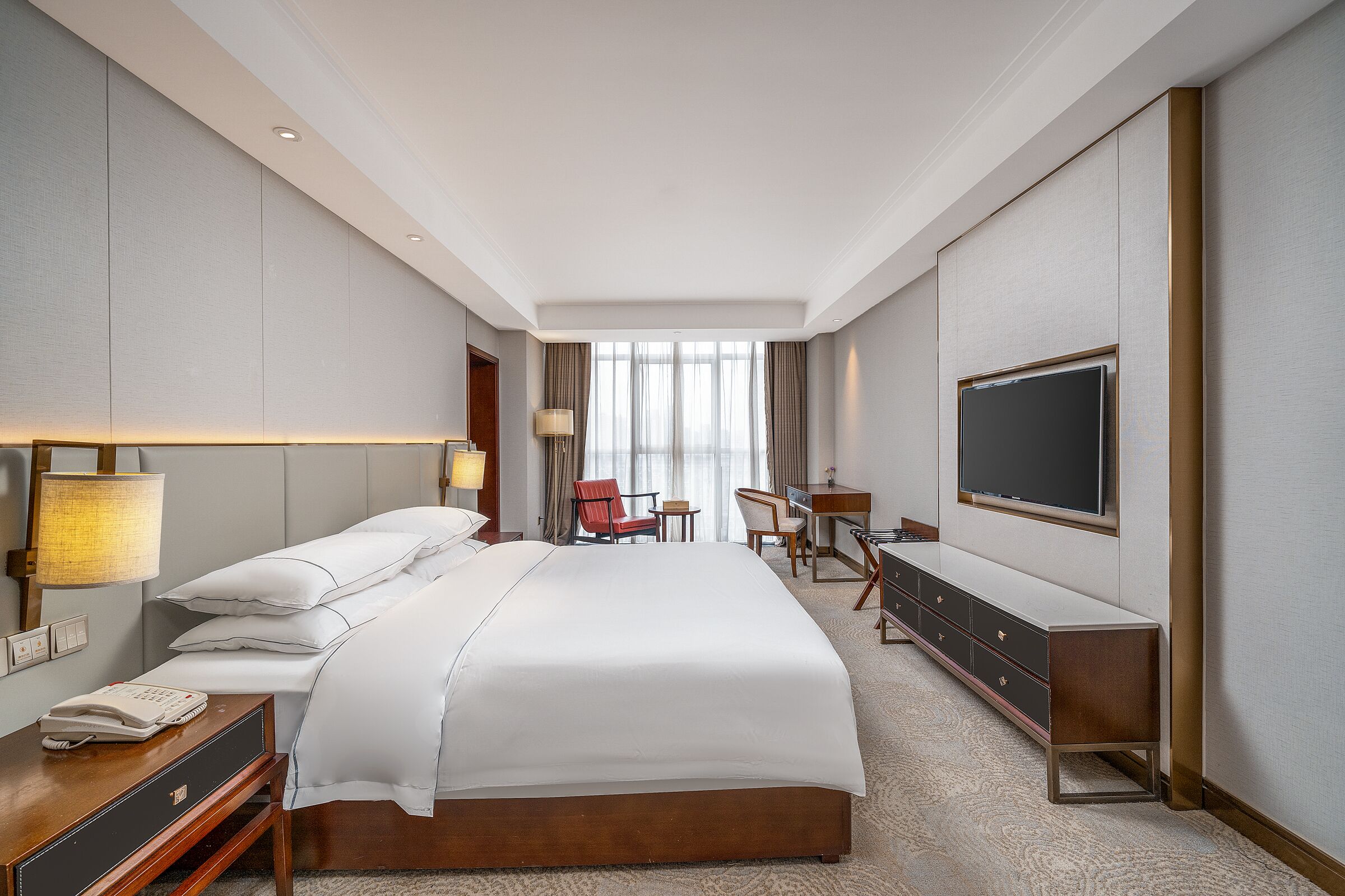 Een hotelkamer met een groot bed, een bureau, een stoel, een televisie en een lamp.