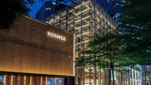 Un edificio moderno con un llamativo letrero de "HERMES" en la fachada, que presenta un diseño geométrico y grandes ventanales.