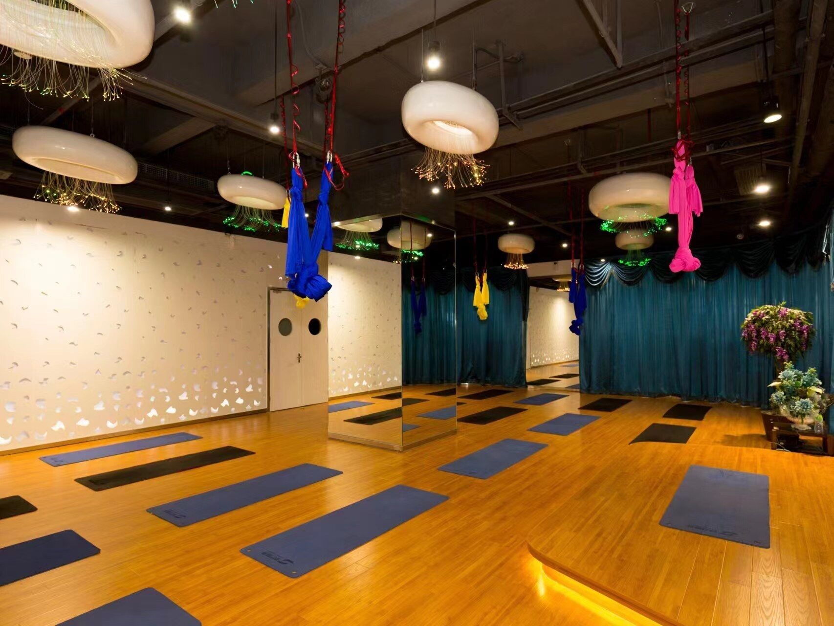 Une pièce spacieuse dotée d’un plancher en bois, de tapis de yoga bleus et de structures en tissu suspendues.