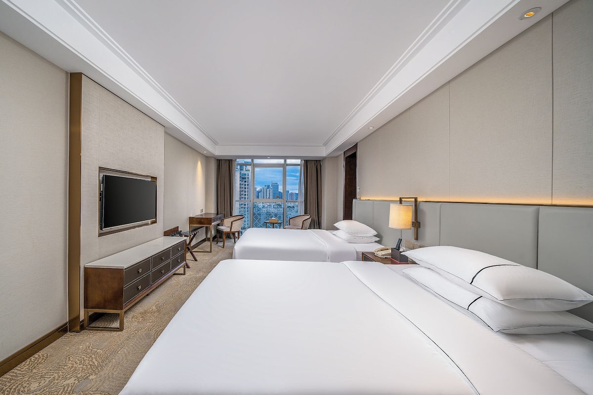 A hotel room with a large bed, a desk, a TV, and a view of the city.