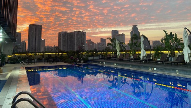 Una piscina en la azotea con vista al horizonte de la ciudad al atardecer.