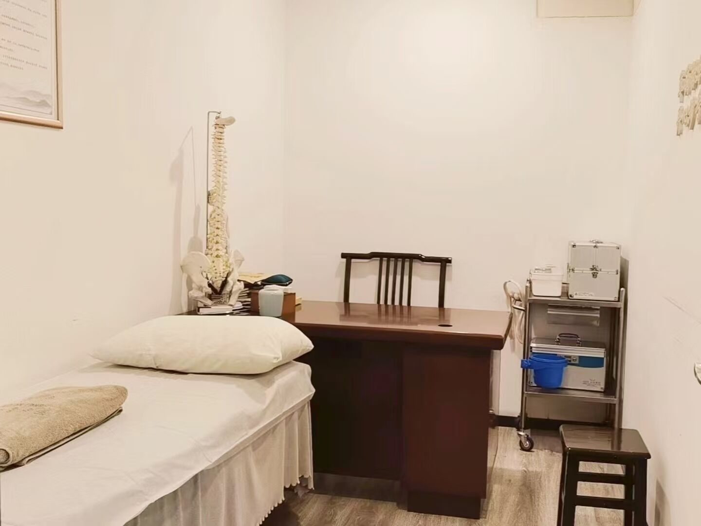 A small, compact room with a bed, a desk, and a chair. There is a shelf with various items on it.