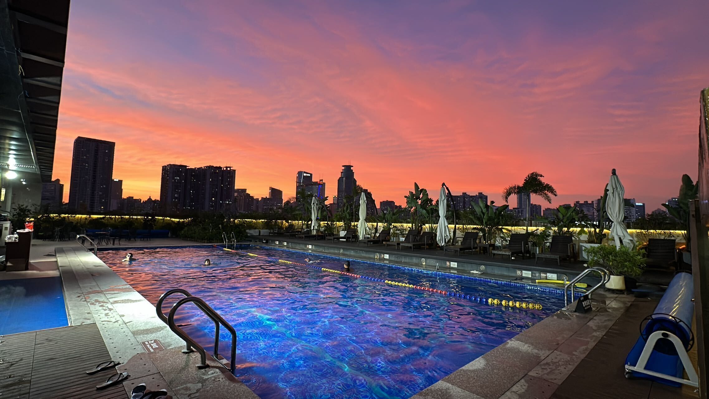 Piscina no terraço com o horizonte da cidade ao fundo durante o pôr do sol.
