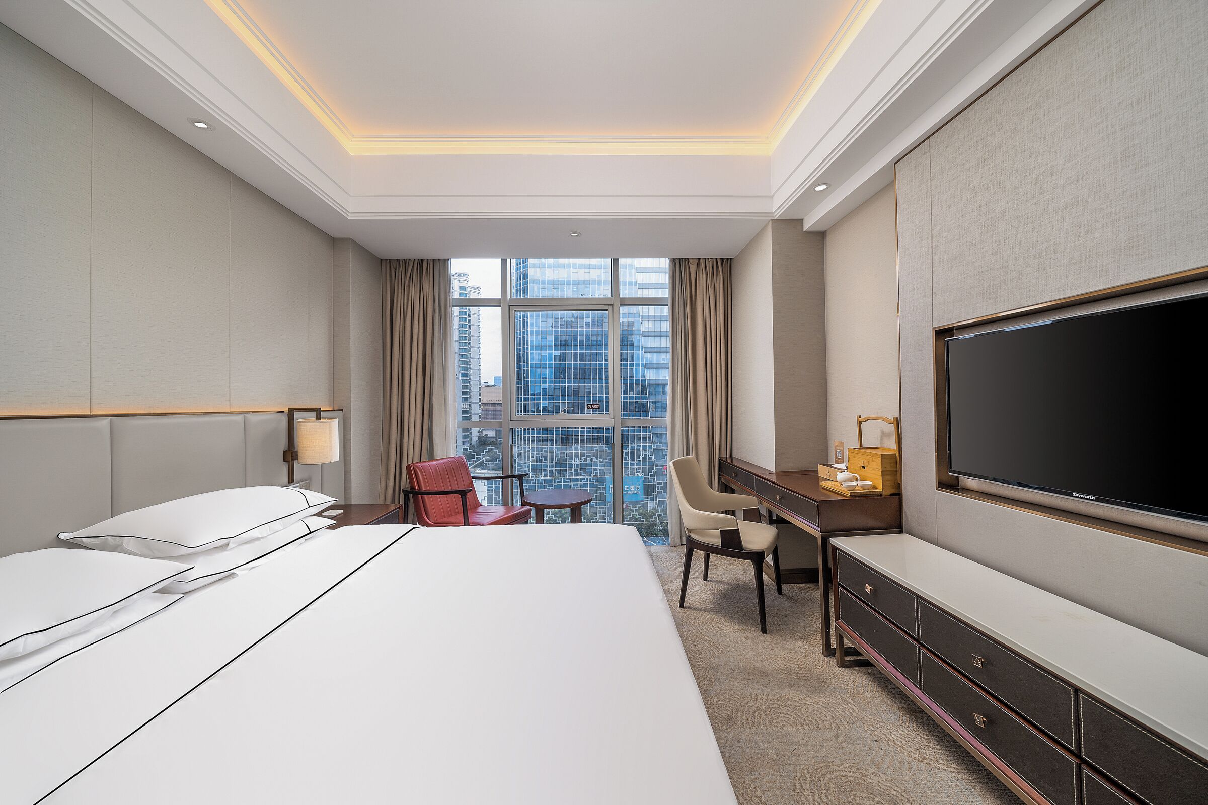 Een hotelkamer met een groot bed, een bureau met stoel, een flatscreen-tv en uitzicht op de stad.