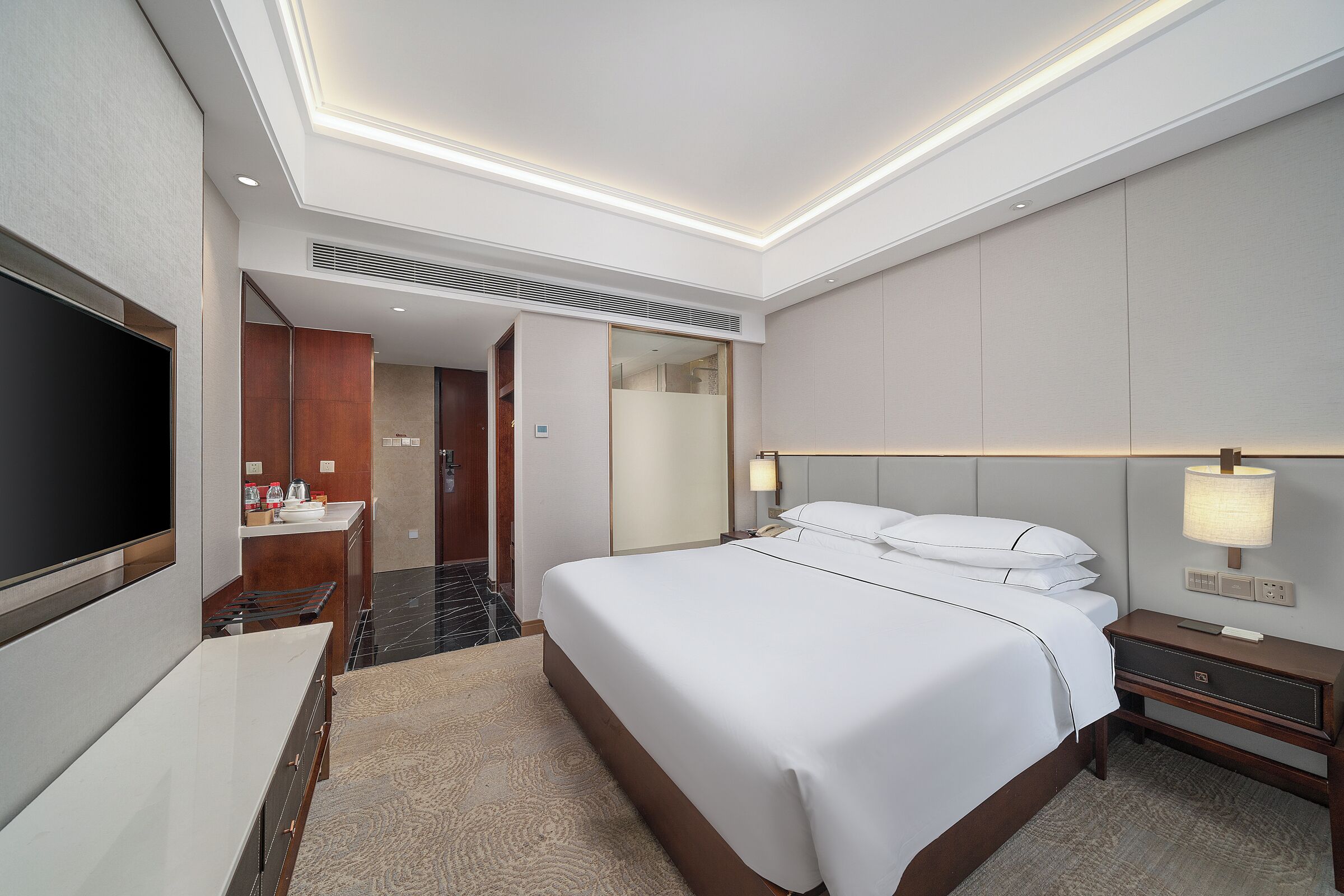 A hotel room with a large bed, bedside table, TV, and a bathroom with a mirror and sink.