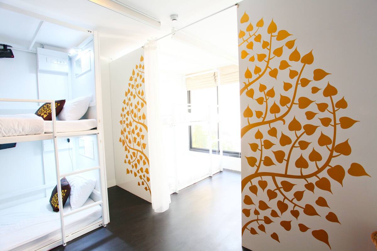 A room with bunk beds, a large window, and a wall with a leaf pattern.