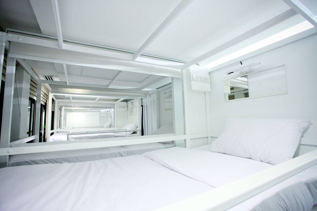 A modern, white-themed hotel room with a large bed, a bedside table, and a mirror on the wall.