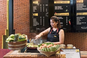 A person preparing food at a counter with a menu board in the background listing coffee, tea, smoothies, and breakfast items.