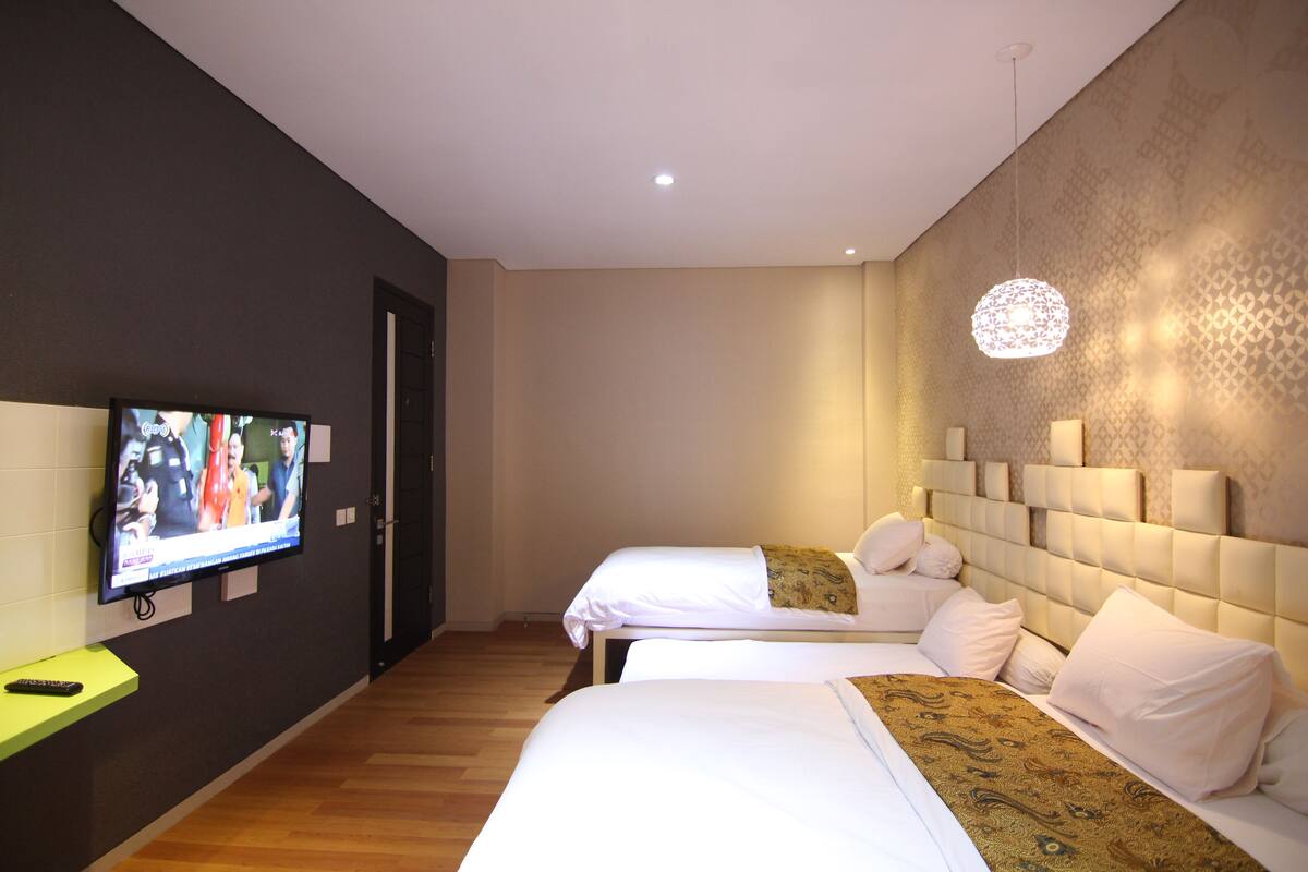 A hotel room with two beds, a television on the left wall, and a patterned wall on the right.
