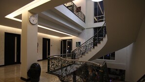 Un intérieur à plusieurs niveaux, avec un escalier en colimaçon, une horloge et une poubelle.