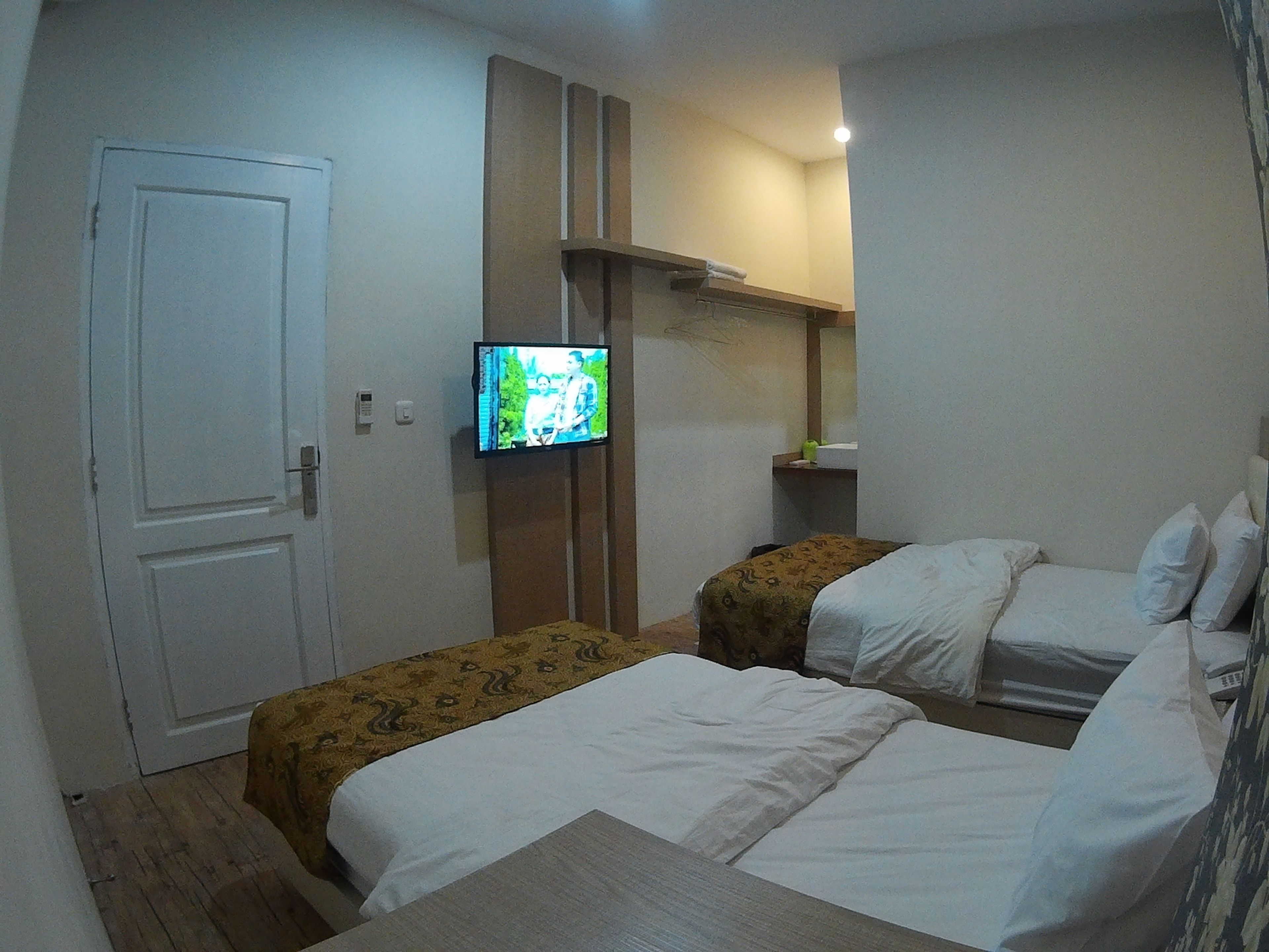 A hotel room with two beds, a television on the wall, and a door.