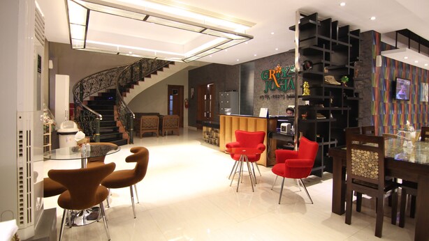 Un hall d’hôtel moderne avec un escalier, des chaises rouges, une table en verre et un comptoir d’accueil.