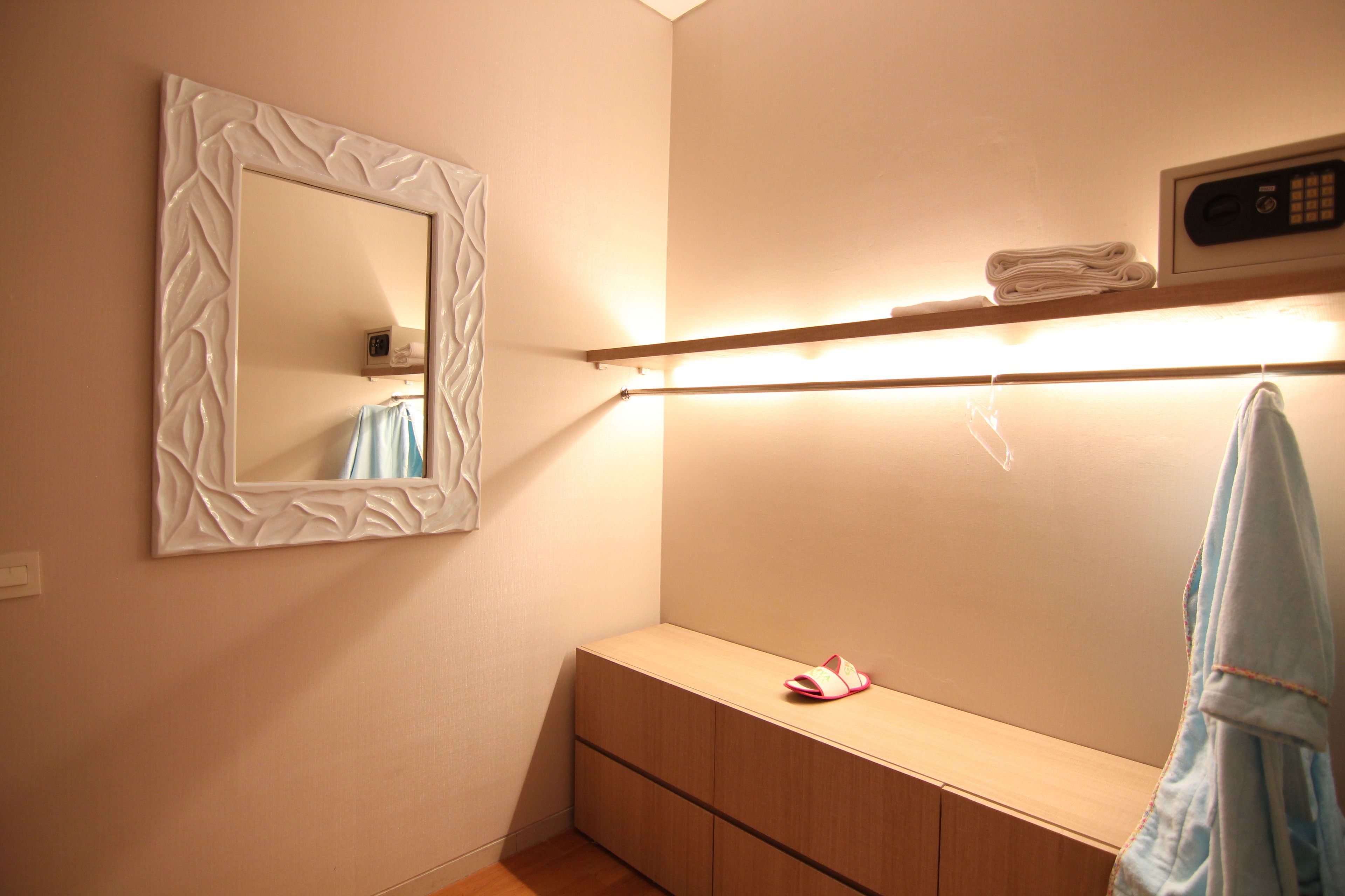 A bathroom with a mirror, a towel rack, a shelf with towels, and a pair of slippers.