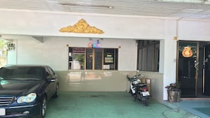 A building with a golden decorative element above the entrance, a signboard with contact information, a parked car, and a motorcycle. - Kedkanok Apartment (Bangkok)