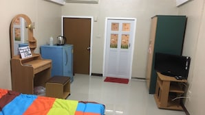A small, well-lit room with a bed, a desk with a mirror, a blue cabinet, a television, and a door with a floral design. - Kedkanok Apartment (Bangkok)