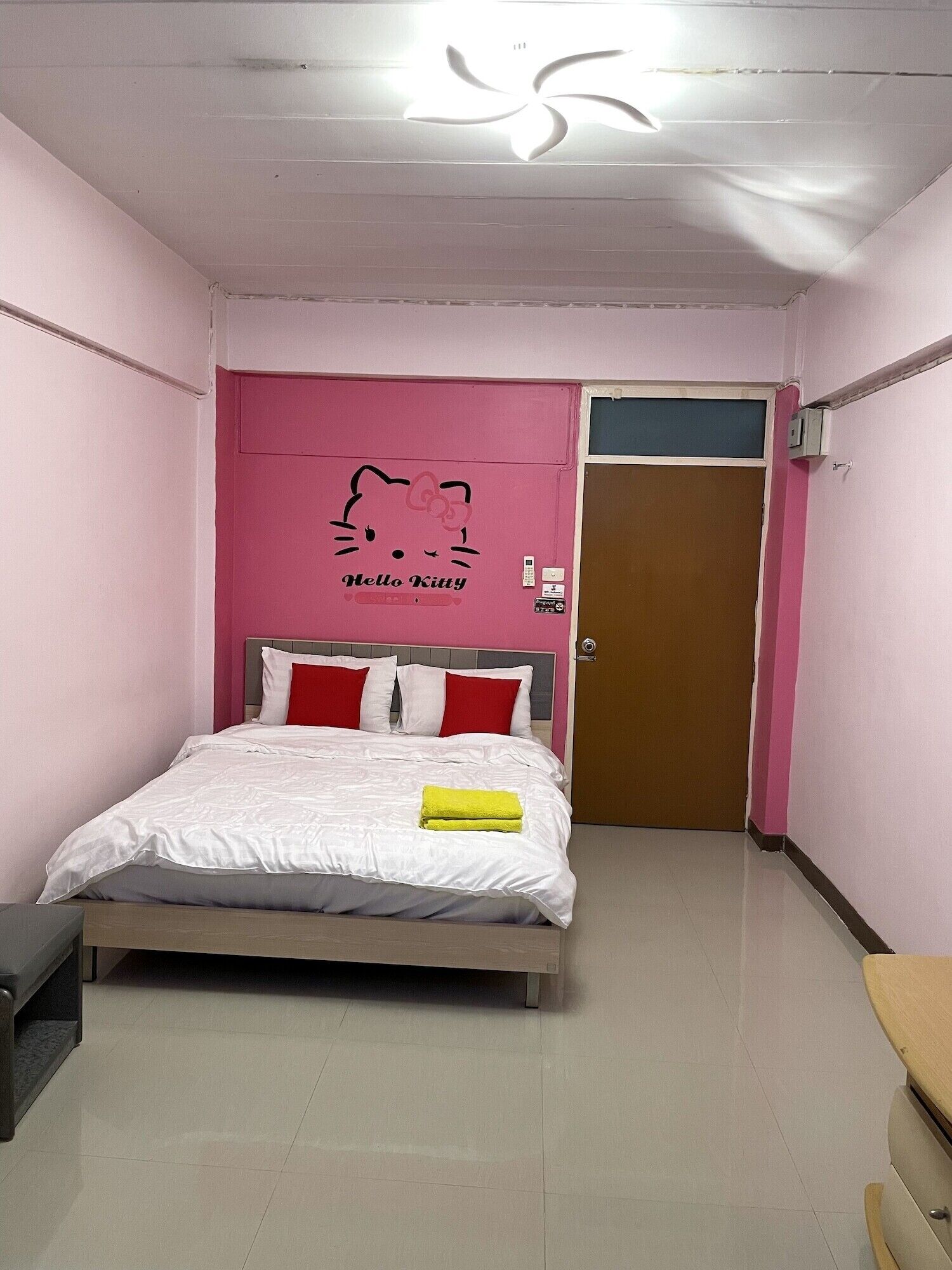 Ett sovrum med en säng, en rosa vägg med en Hello Kitty-dekal, en dörr och en taklampa.